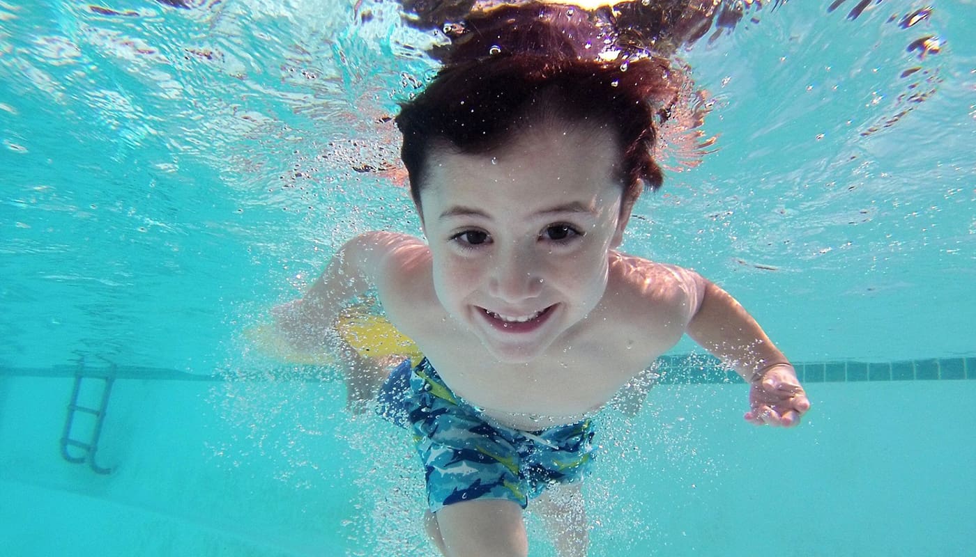 A little boy is smiling while swimming in a pool.