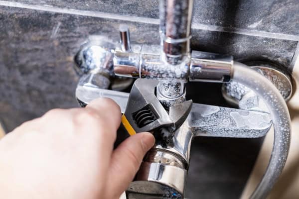 Close-up of a plumber’s hands repairing a leaking kitchen faucet with a wrench.