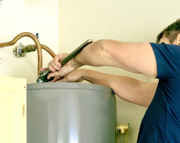 Technician using a wrench to repair plumbing connections on top of a residential hot water tank